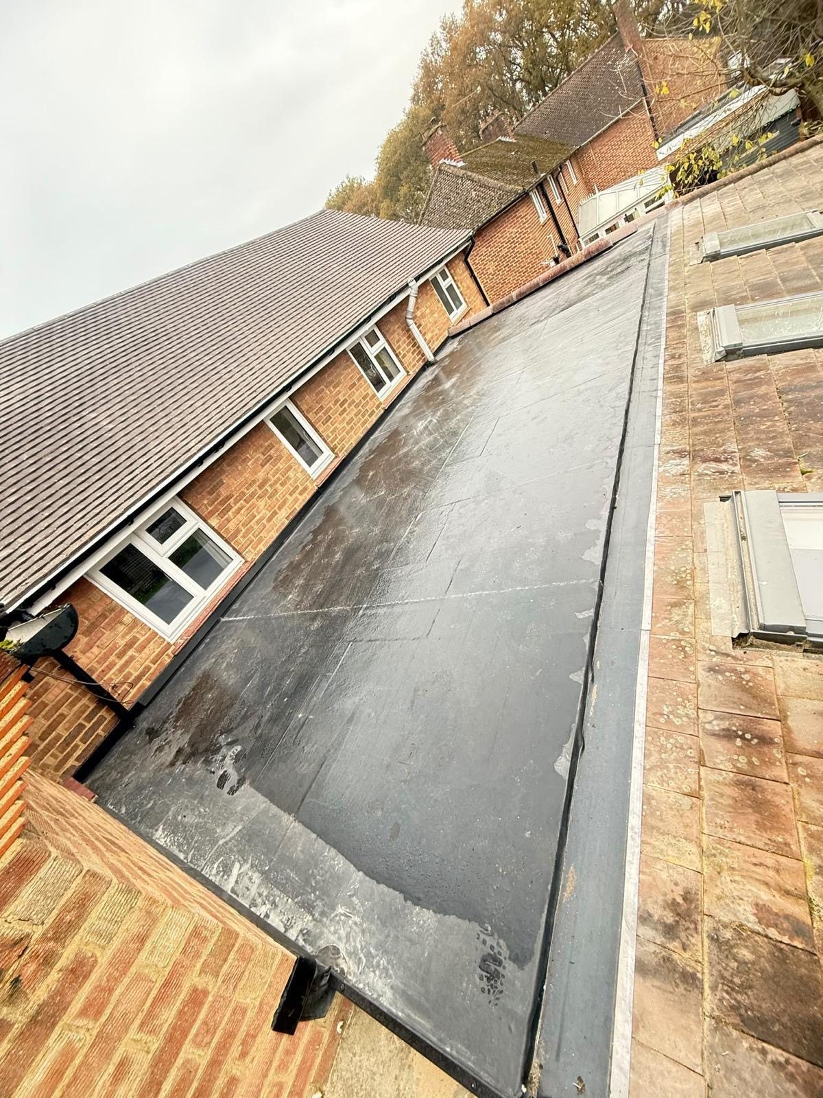 New black EPDM rubber flat roof running between a brick bungalow and a tiled roof with roof windows