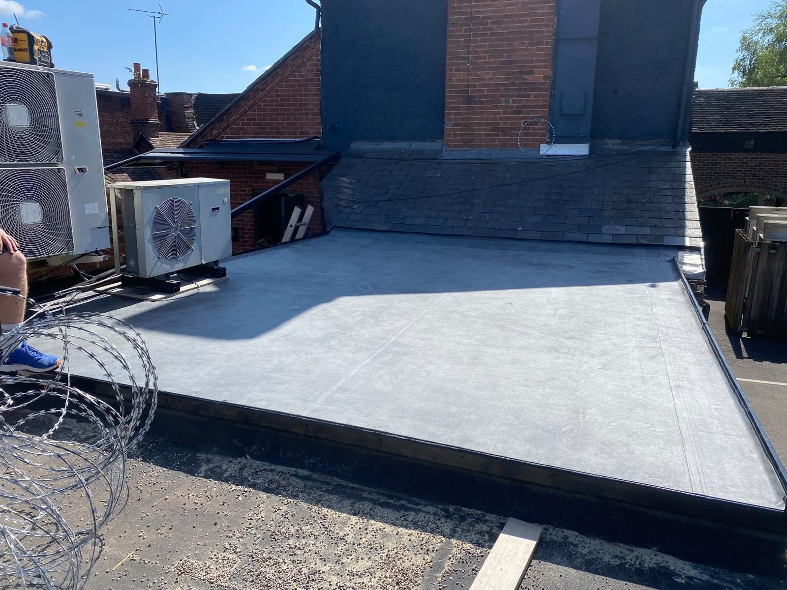 New grey EPDM flat roof with a slate-hung upstand and air-conditioning units, in sunshine