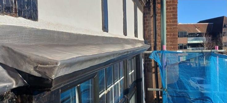 Close-up of a new lead-covered canopy over a bay window, with scaffold netting alongside