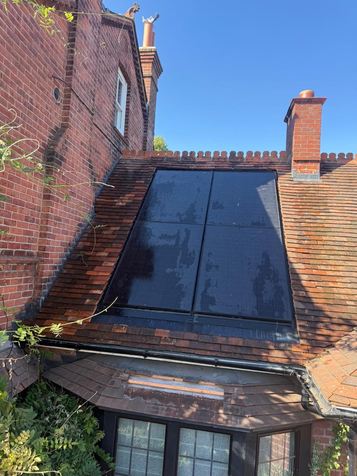 Black in-roof solar panels on an old red clay plain-tile roof of a brick house, with chimneys